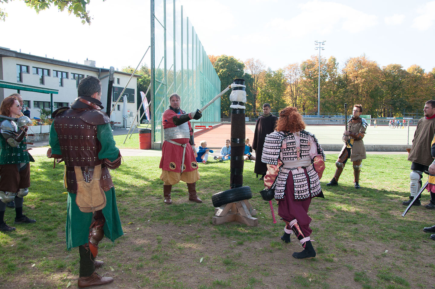 Ein Mann in Rüstung ohne Helm steht an einer Säule und zeigt mit einem Schwert eine Übung vor